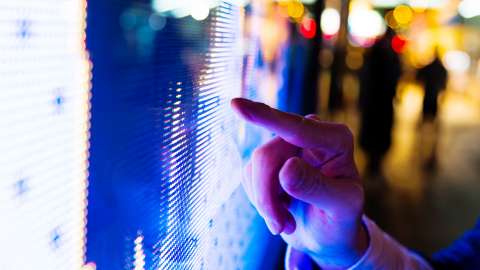 Man's finger pointing at LED screen of stock market price at night